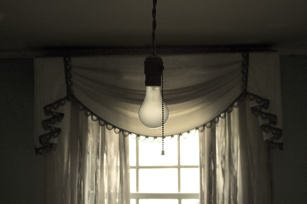 bare lightbulb with chain in front of window and fancy curtain