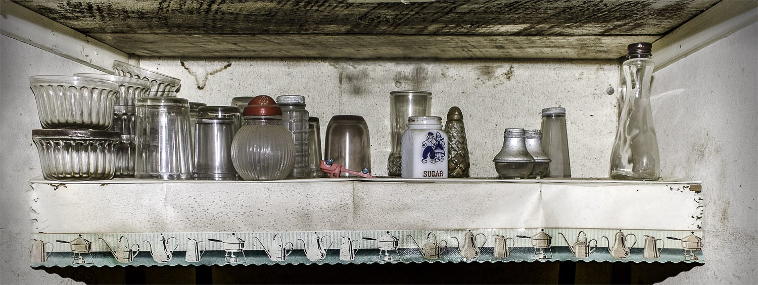 Pantry shelf with stains, dishes, a very small sugar container and a tiny toy truck.
