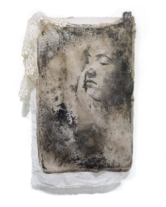 face of a woman with eyes closed embedded in acrylic and surrounded by fabric.