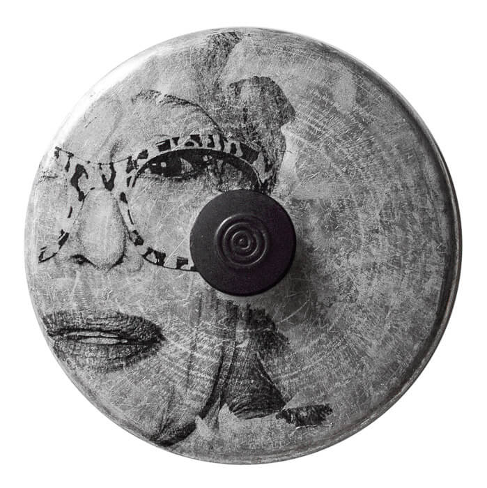 a photo image transfer of an older woman with large fun glasses on a pot lid with lots of circles on the metal and the handle