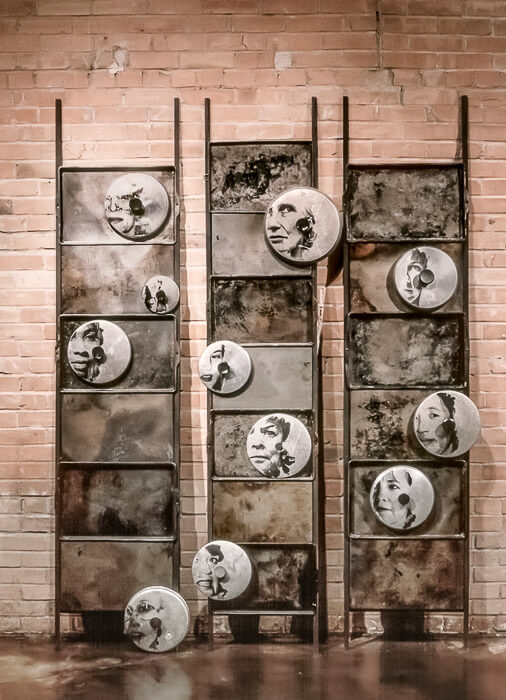 pot lids with faces mounted on 3 panels of old charred pans