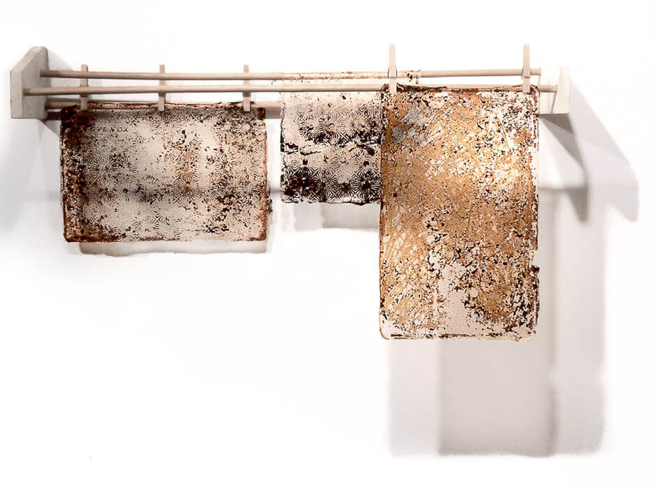 Conceptual art consisting of 3 skins of acrylic polymers with rust, carbon and markings (from old bakeware) hanging on an old rack with clothespins, Sally Mankus