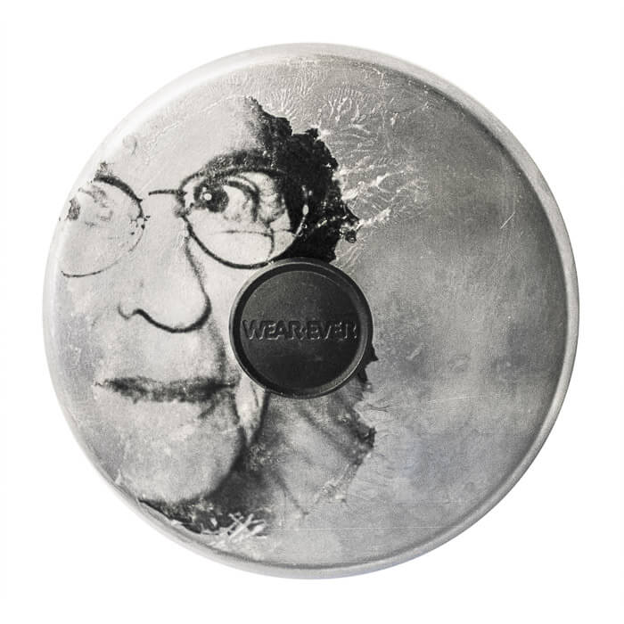 a woman with glasses looking out on a metal pot lid (with a WearEver handle)