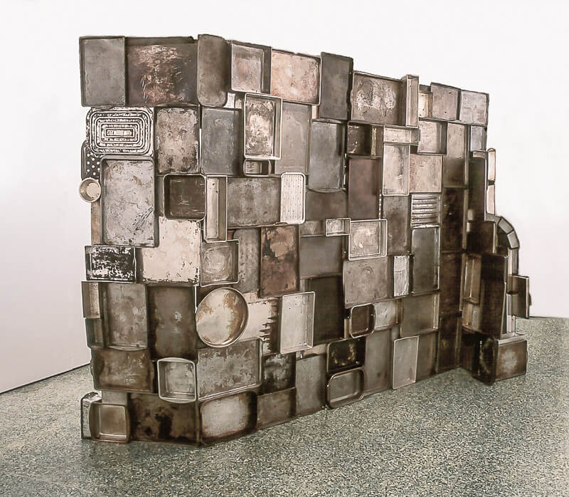 a sculpture made of found objects, pans, bound together to make a free standing wall